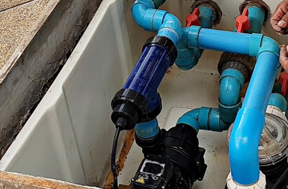 Pool cleaning equipment including brush, vacuum head, skimmer net, and hose placed beside a backyard swimming pool at sunset.